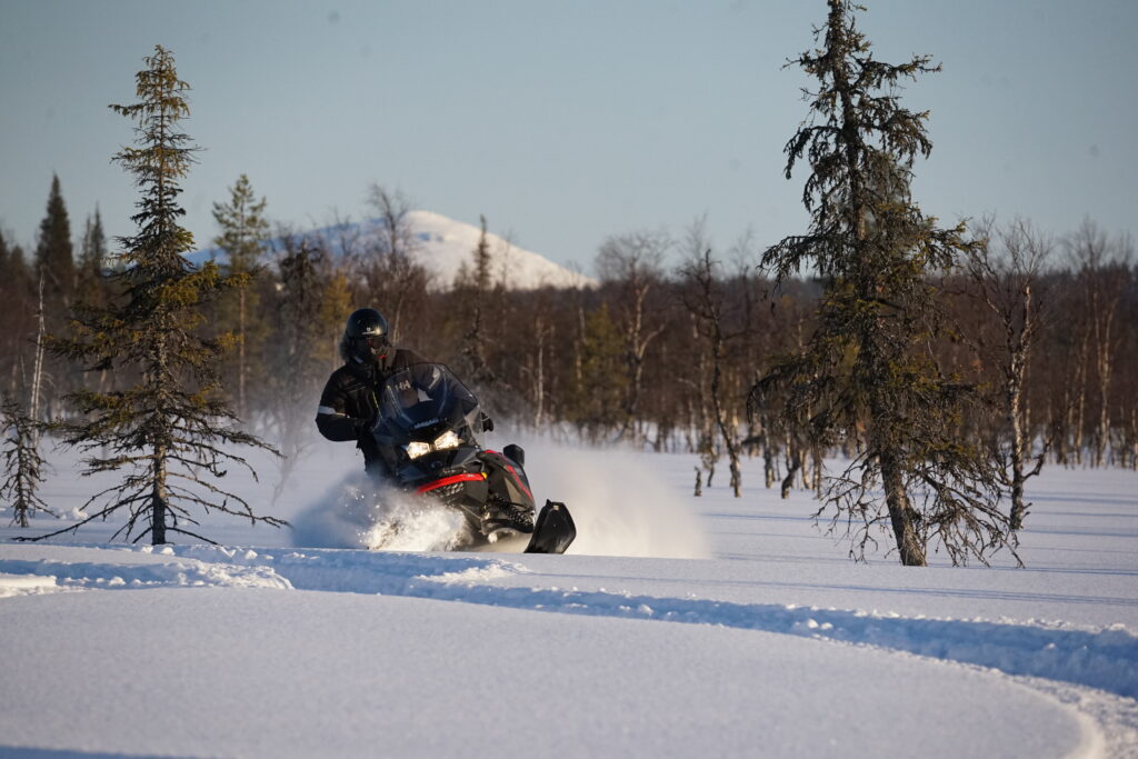 Pilote en motoneige traversant une forêt enneigée à grande vitesse, lors d’un raid hivernal dans le Grand Nord