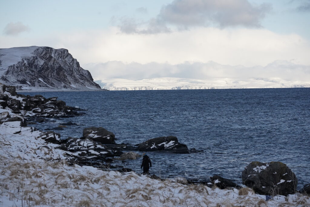 Participant à un raid motoneige sur la côte arctique enneigée, face à la mer glacée et aux falaises escarpées