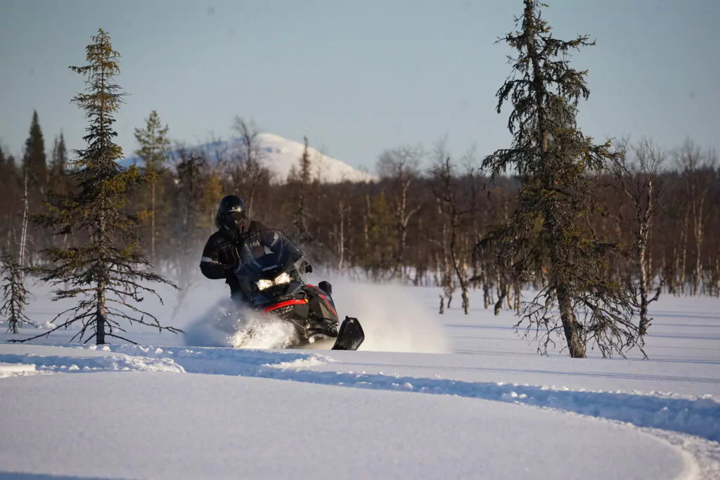 Pilote en motoneige traversant une forêt enneigée à grande vitesse, lors d’un raid hivernal dans le Grand Nord