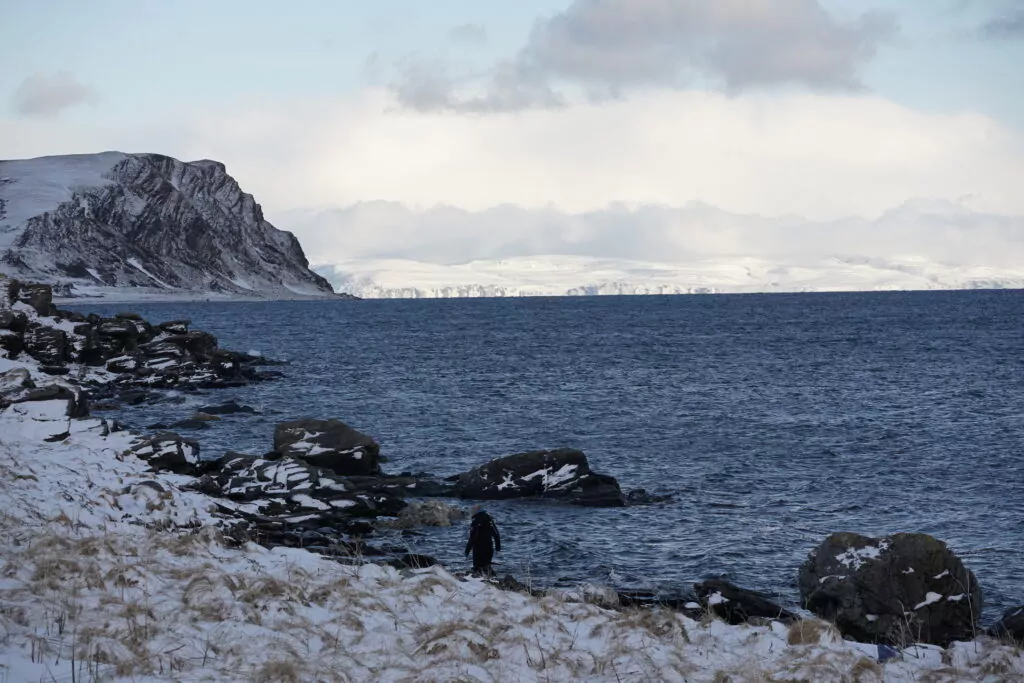 Participant à un raid motoneige sur la côte arctique enneigée, face à la mer glacée et aux falaises escarpées